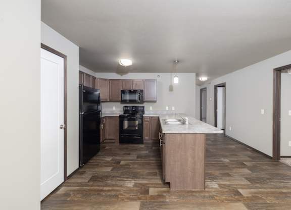 A kitchen with black appliances and a wooden floor.