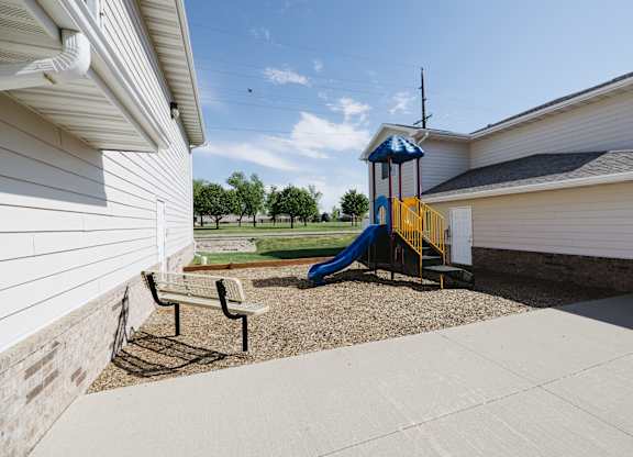 A playground with a blue and yellow slide in the middle of a concrete area.