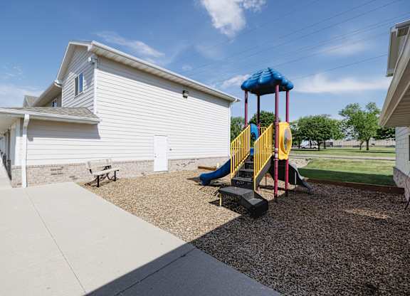 A playground with a slide and a white house in the background.