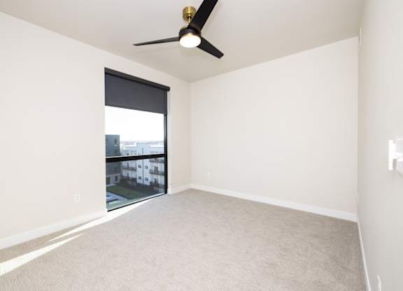 A room with a ceiling fan and a window overlooking a building.