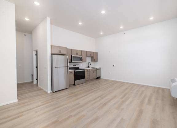 A kitchen with white walls and wooden floors with a refrigerator, microwave, oven, and sink.