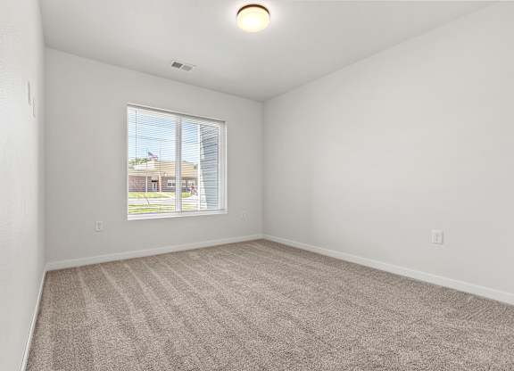 A room with a carpeted floor and a window showing a view of a building outside.