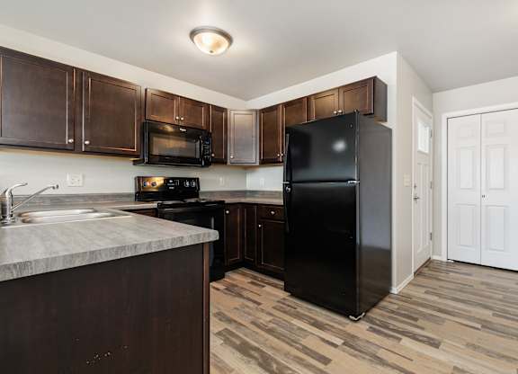 A black refrigerator in a kitchen with wooden cabinets and a marble counter.
