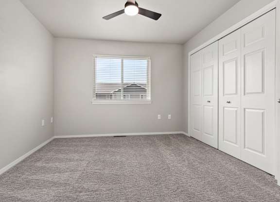 A room with a ceiling fan and a window with blinds.