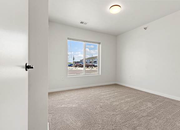 A room with a carpeted floor and a window overlooking a parking lot.
