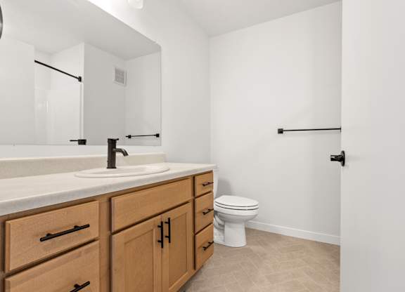 A white toilet sits in a bathroom with a sink and wooden cabinets.