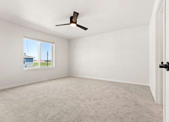 A room with a ceiling fan and a window showing a blue sky and a building.