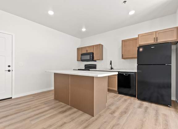 A kitchen with a black fridge and microwave above a counter.