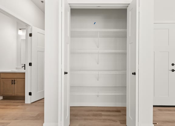 A white pantry with a door open to a white hallway.