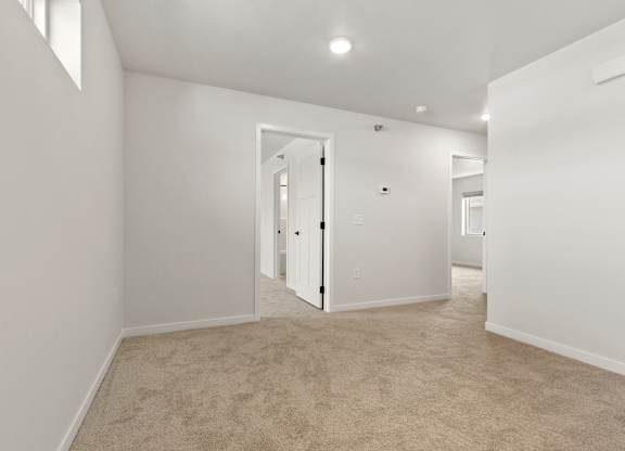 A white room with a carpeted floor and a doorway leading to another room.