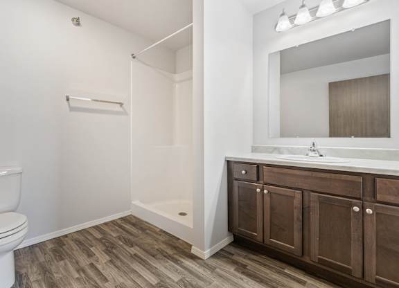 A white toilet sits in a bathroom with wood flooring and a white sink.
