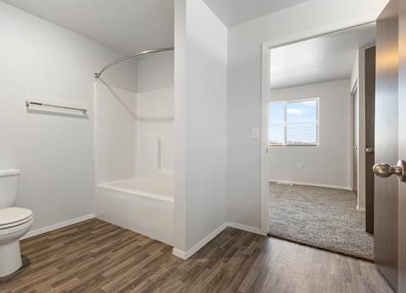 A white toilet sits next to a bathtub in a bathroom with wood flooring.