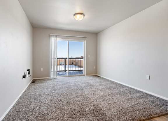 A room with a carpeted floor and a sliding glass door leading to a balcony.