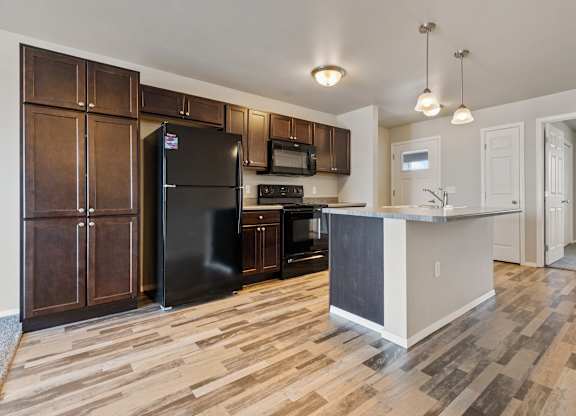 A kitchen with a black refrigerator and wooden cabinets.