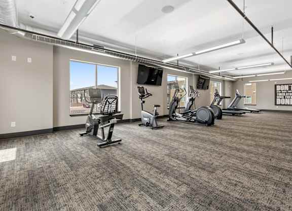A gym with a variety of exercise equipment and a motivational poster on the wall.