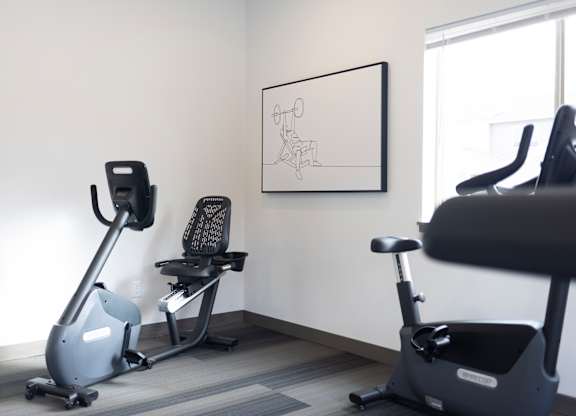 A room with a stationary bike, a rowing machine, and a framed drawing on the wall.