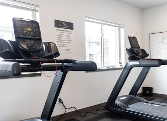 Two treadmills are in a gym with a sign that says "Fitness Center Rates.".