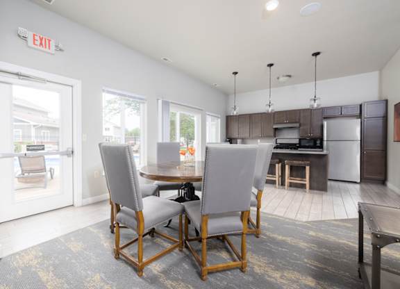 A kitchen with a dining table and chairs in the foreground and an exit sign on the wall.