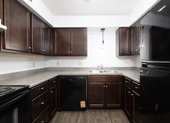 A kitchen with dark wood cabinets and black appliances.