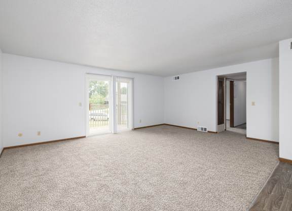 A spacious room with carpeted floor and sliding glass doors.