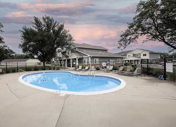A large outdoor swimming pool surrounded by a fence and a house in the background.