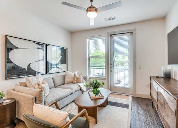 A living room with a grey couch, a wooden table, and a ceiling fan.