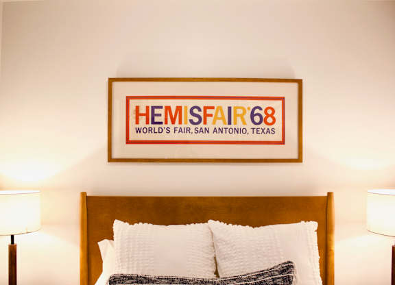 A bedroom with a bed and a framed poster of HEMISFAIR'68 on the wall.