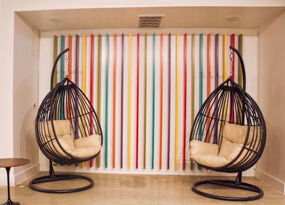 Two hanging chairs in front of a colorful striped wall.