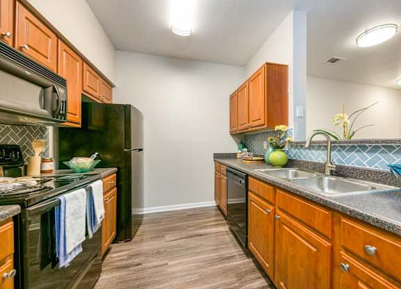 a kitchen with black appliances and wood cabinets at Sunrise Canyon, Universal City, TX