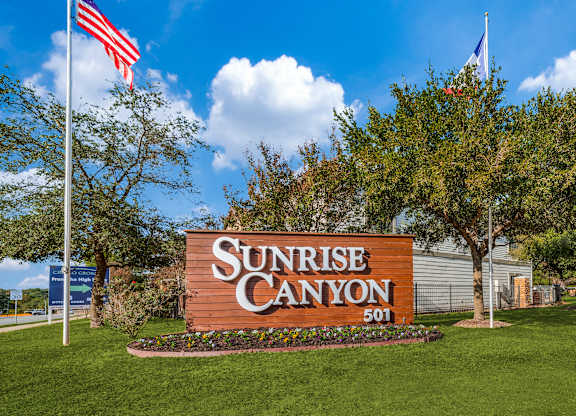 a sign with the words sunrise canyon on it and an american flag flying in the background at Sunrise Canyon, Universal City, Texas