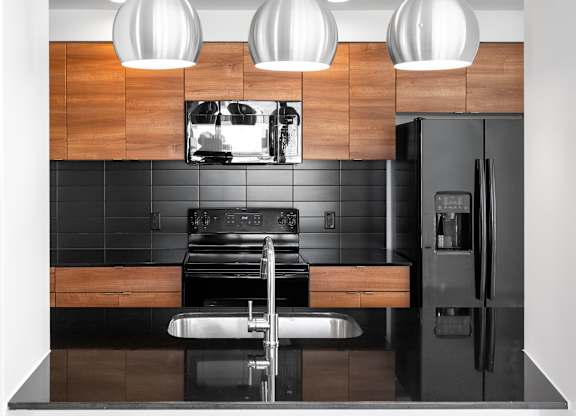Modern kitchen with wood cabinetry and black backsplash at THE'68 Apartments, San Antonio, Texas