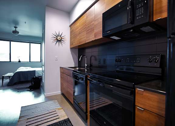 Contemporary kitchen with black appliances and wood finishes at THE'68 Apartments, San Antonio