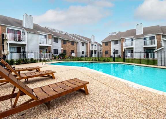 a swimming pool with two wooden benches next to an apartment building at Northchase, Austin, TX