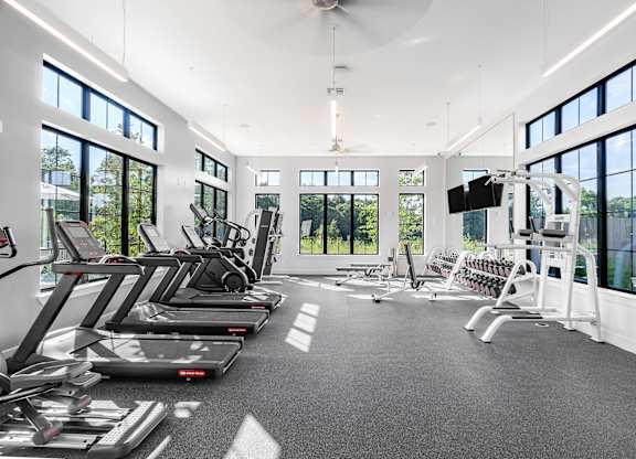 A gym with treadmills, elliptical machines, and a flat screen TV.