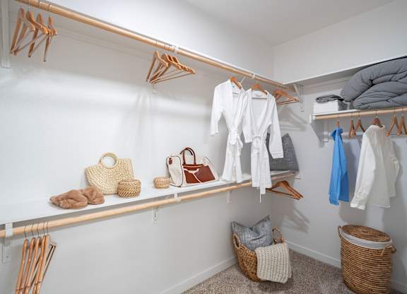 A white closet with clothes and baskets.