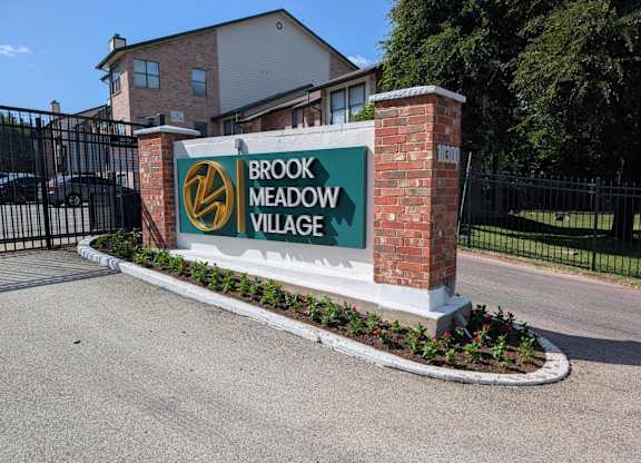 A sign for Brook Meadow Village stands in front of a gated entrance.