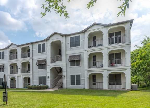A large white apartment building with multiple balconies and a green lawn in front at Rosemary Apartments, Conroe, Texas