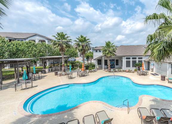 A large outdoor swimming pool surrounded by lounge chairs and palm trees at Rosemary Apartments, Conroe, TX, 77384