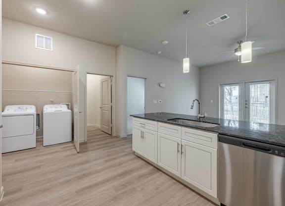 Kitchen with laundry room and dark countertops at Emilia Apartments, Boerne, TX