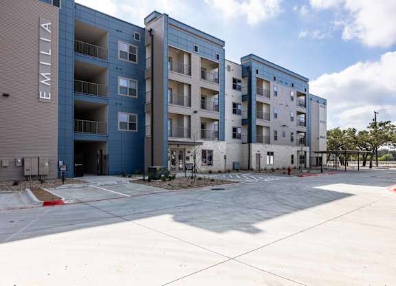 Modern apartment building exterior with parking area at Emilia Apartments, Texas