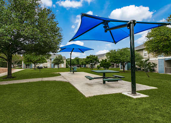 a picnic area with picnic tables and umbrellas  at Rosillo Creek Apartments, San Antonio, TX