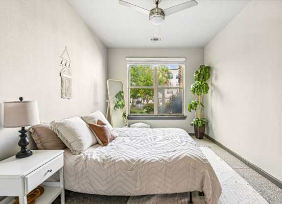 A bedroom with a bed, a ceiling fan, and a window with a view of trees.