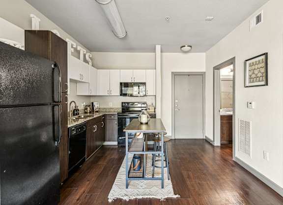 A kitchen with a black fridge and wooden floors.