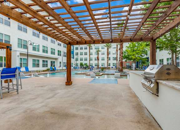 A wooden pergola over a pool area with a chair and a table.