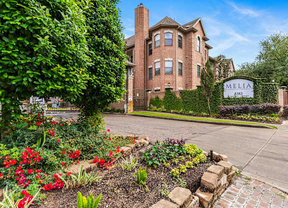 Property entrance with landscaped flower beds and signage at Melia Medical Center Apartments, Houston