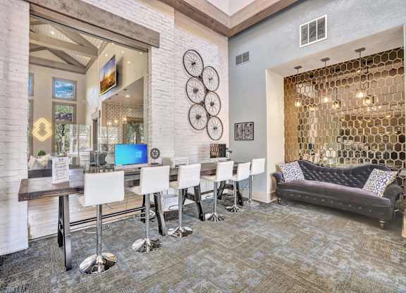 A modern office space with a grey sofa, a wooden table and chairs, and a glass wall.