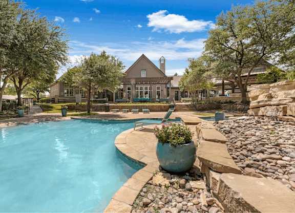 A large outdoor swimming pool surrounded by a stone wall and a large pot of flowers.