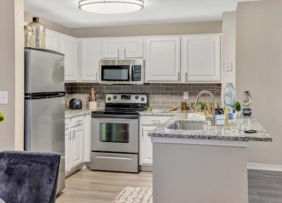 A kitchen with a refrigerator, microwave, oven, and sink.