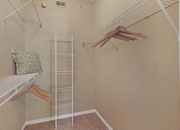 A room with a white shelf and clothes hanging on a rack.