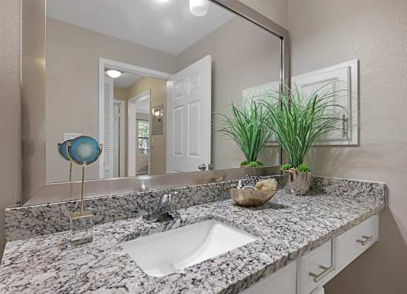 A bathroom with a marble countertop and a round mirror.